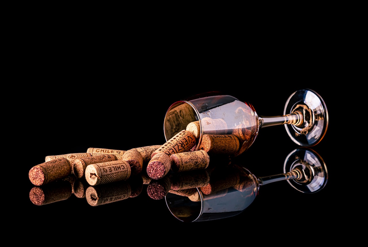 An open wine bottle with a cork beside it and a half-empty glass