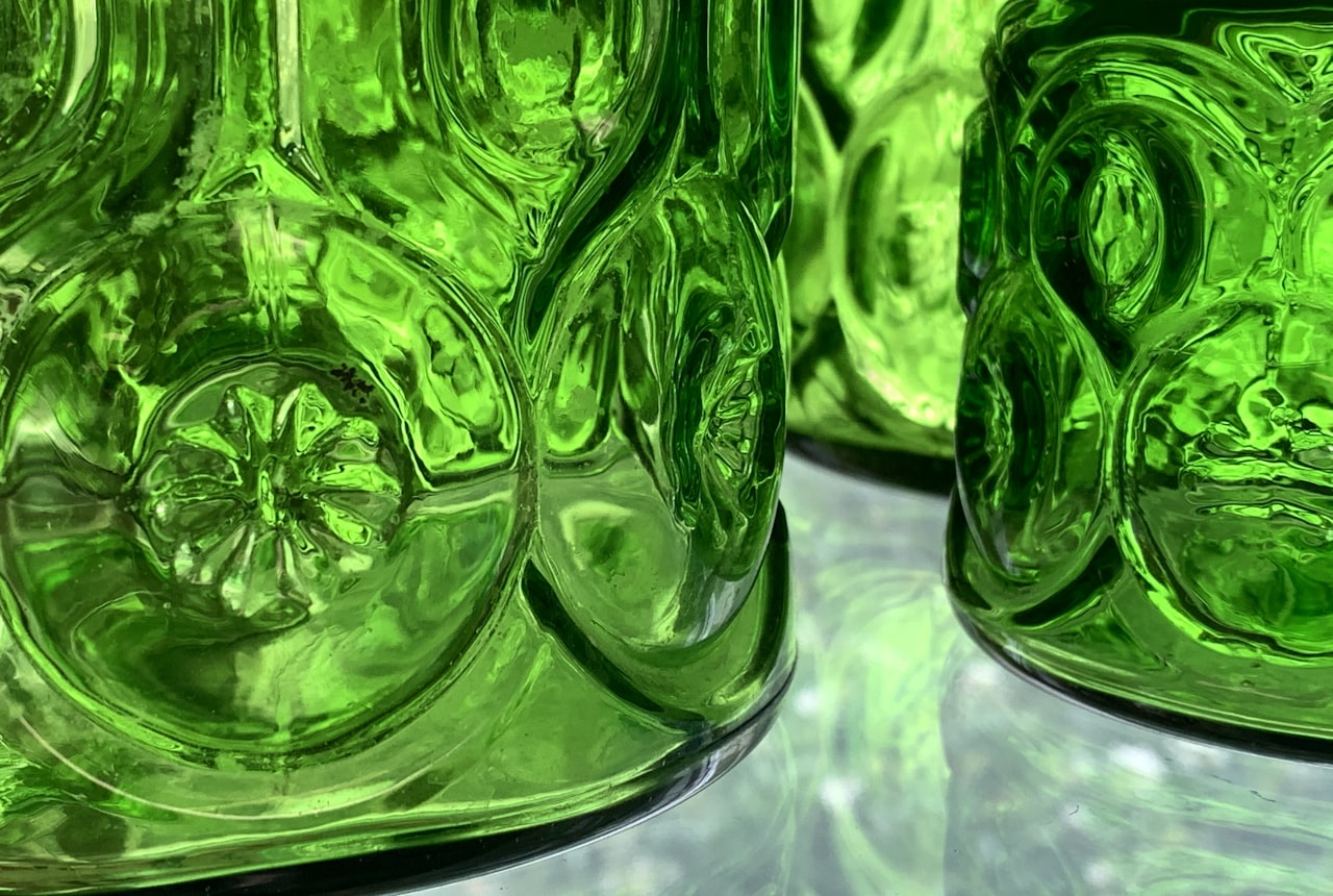 Side-by-side bottles in different glass colors — dark green, brown, light green, clear — on a wooden surface with backlight