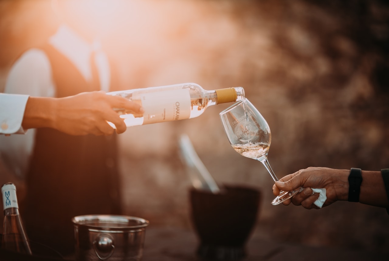 Wine being poured from a bottle into a glass decanter, deep ruby liquid catching the light