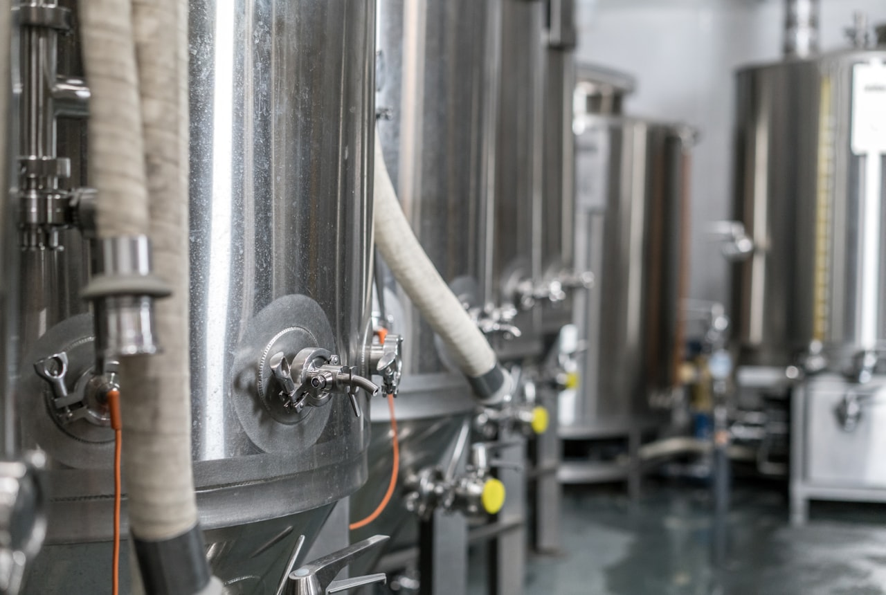 A row of stainless steel fermentation tanks with hatches open, frothy red wine bubbling visibly