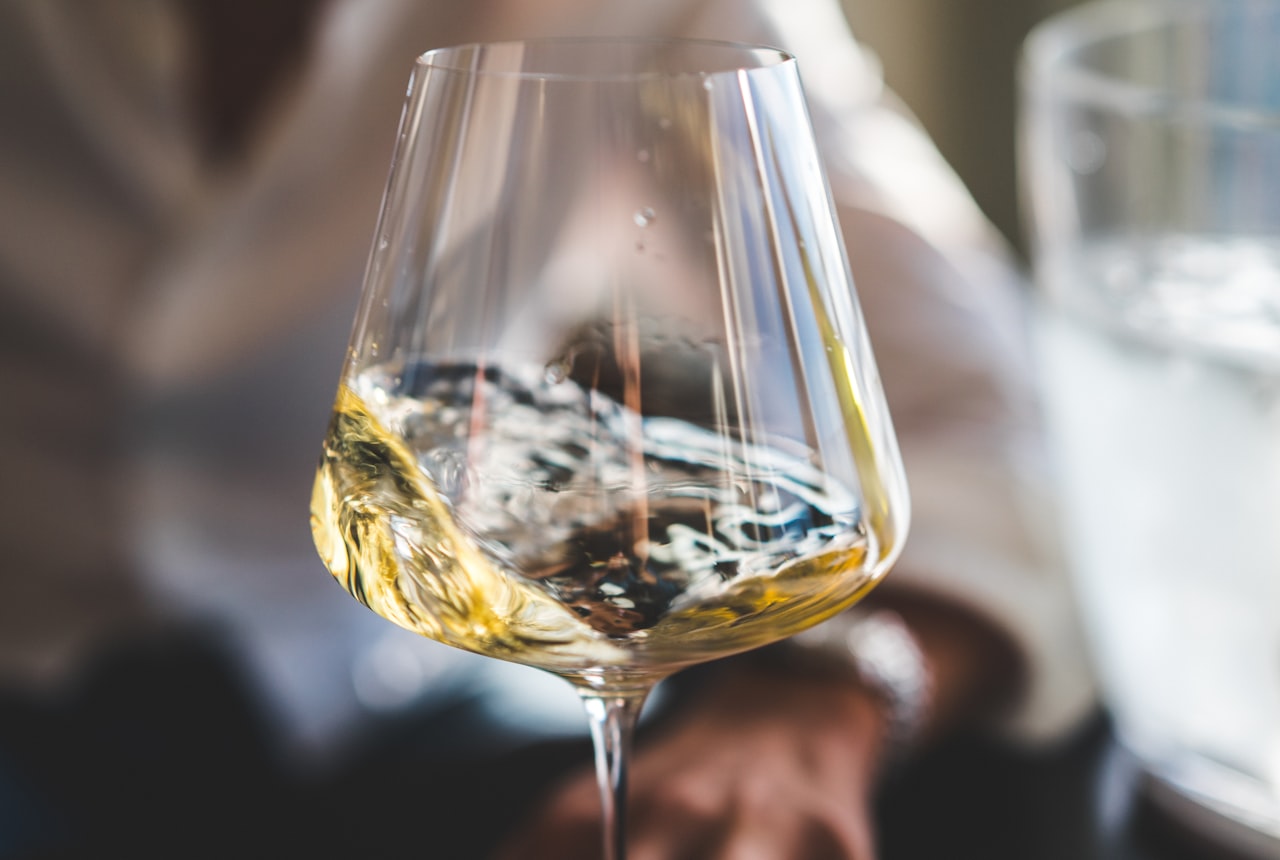 A hand holding a wine glass against a soft white tablecloth, light catching the rim