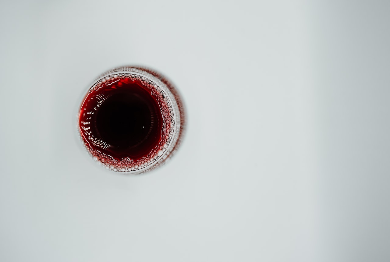Hand swirling a glass of red wine with motion blur and droplets forming on the inside, dramatic side-light