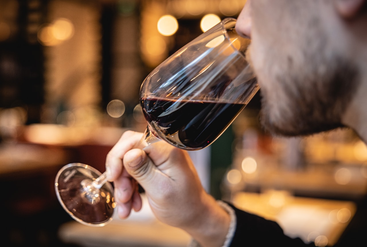 Close-up of a person's nose hovering above a wine glass, eyes closed, soft warm light