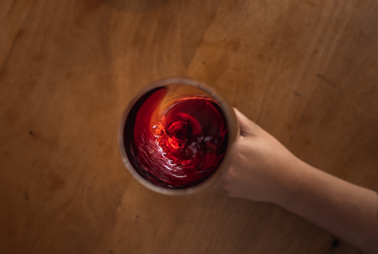 A glass of red wine half empty on a wooden table, evening light, contemplative scene