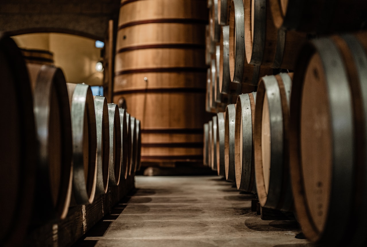 Stacked oak wine barrels with a large foudre in a dim cellar