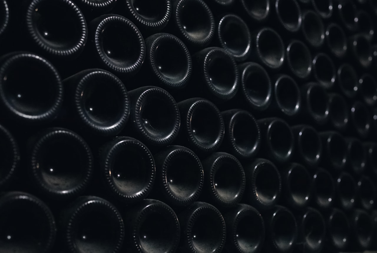 A row of wine bottles lying horizontally on a wooden shelf in a softly-lit dark hallway closet