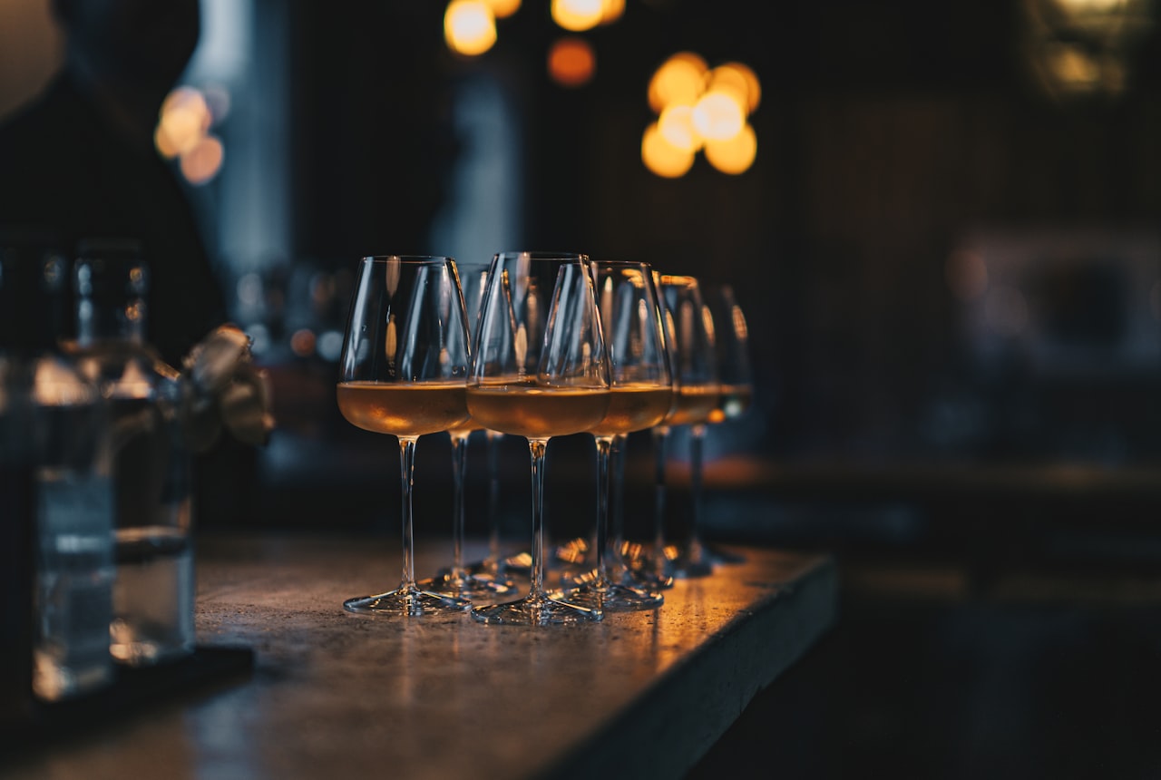 Five glasses in a row on a long dark wood table, editorial composition