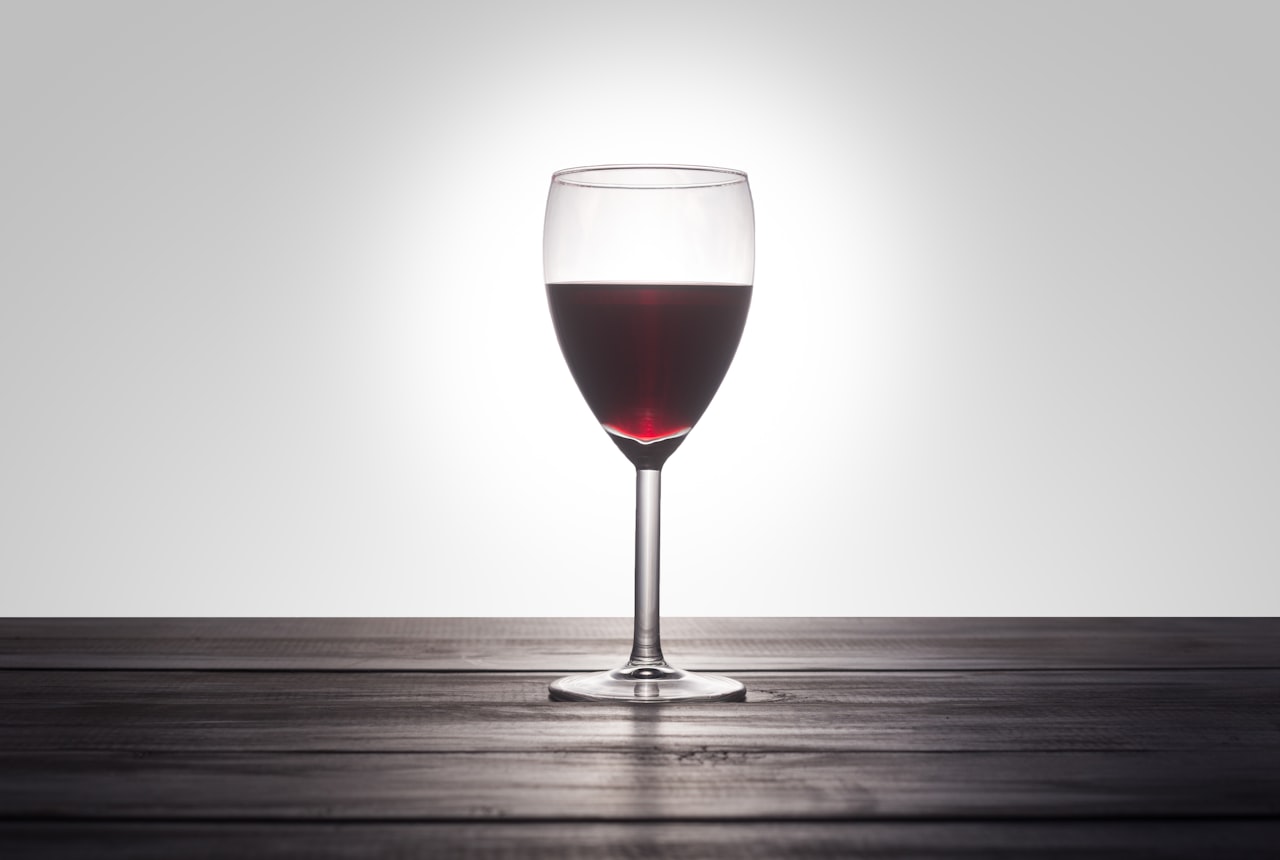 A single Bordeaux-shaped glass with deep ruby wine, dramatic warm light on dark wood
