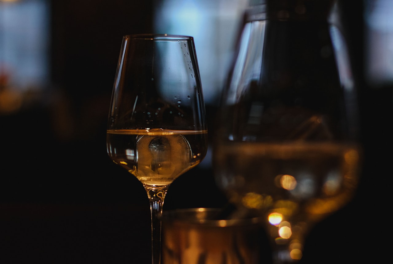 A single white wine glass with pale golden wine, condensation on the bowl, fresh daylight